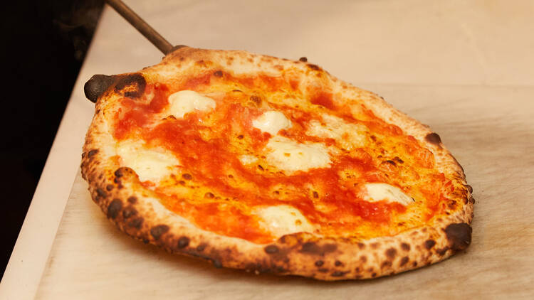 A margherita pizza is pulled from the pizza oven and laid on a kitchen bench