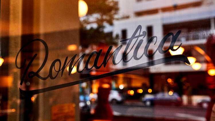 The word 'Romantica' is written in black italic print on the front window of the bar