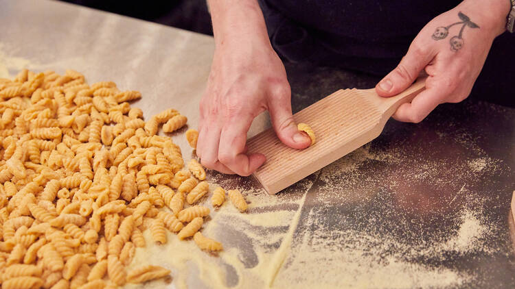 A person hand-makes pasta on a floured silver bench 