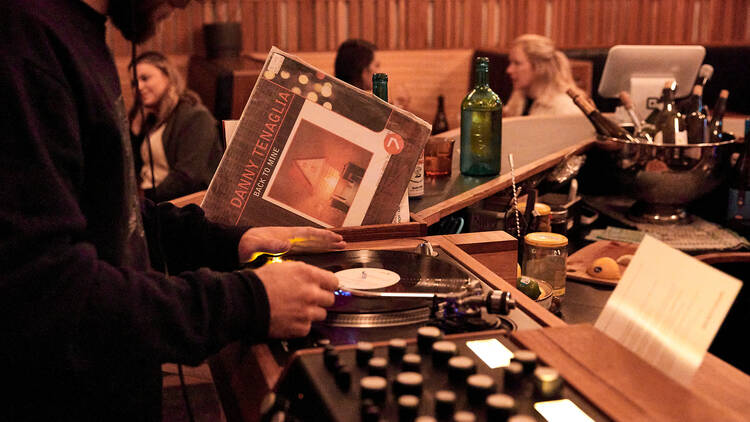 A DJ changes a vinyl record with a Danny Tenaglia record sitting next to the record player
