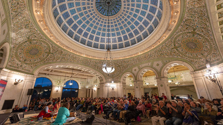 A crowd gathers beneath the green Tiffany dome to watch Indian classical music performers onstage at Ragamala