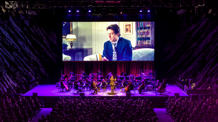 A concert hall with an orchestra playing in front of a screen