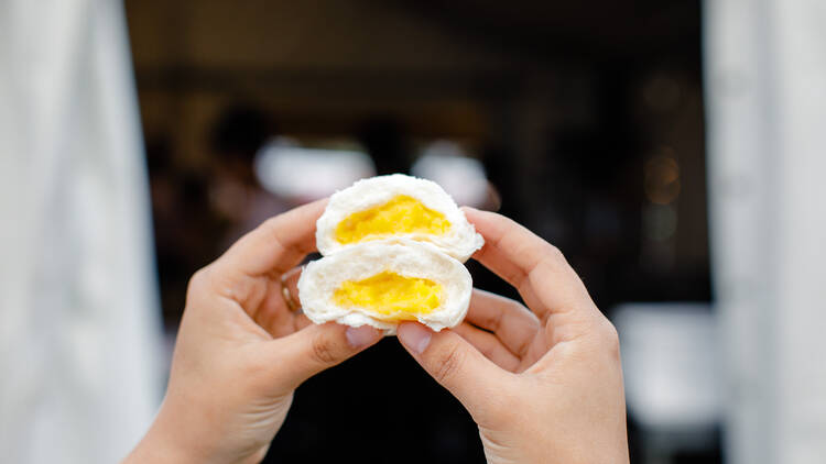 A person holds a custard egg bun broken in half