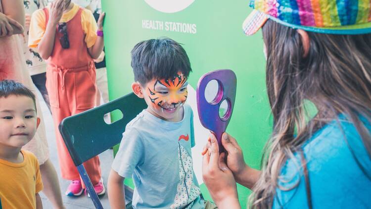 A little boy with his face painted to look like a tiger checks himself out in a handheld mirror.