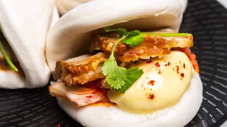 Bao buns filled with crispy pork and mayonnaise sit on a black plate