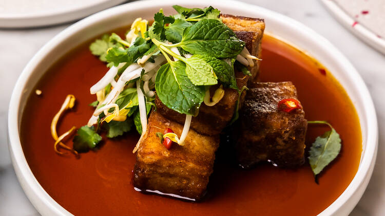 A plate of crisy pork belly topped with herb salad and sauce on a white plate