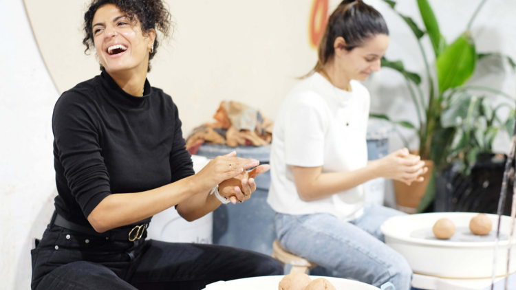 Two women laugh while moulding balls of clay in their hands 