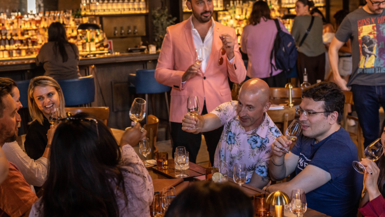 A man in a pink jacket stands above a table full of people clinking their drinks
