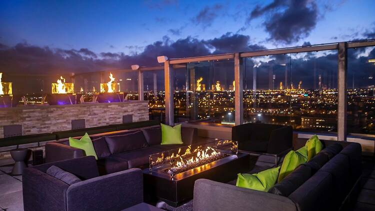 Black couches surround a fire pit with skyline views in the background 