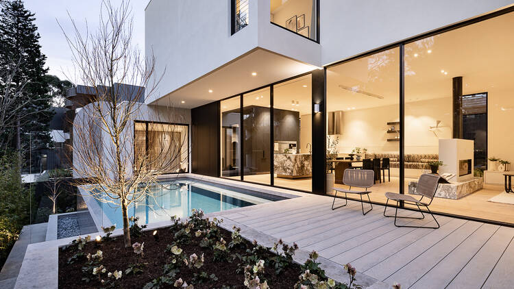 The outside of a home with a pool, shrubs and glass doors looking into the kitchen