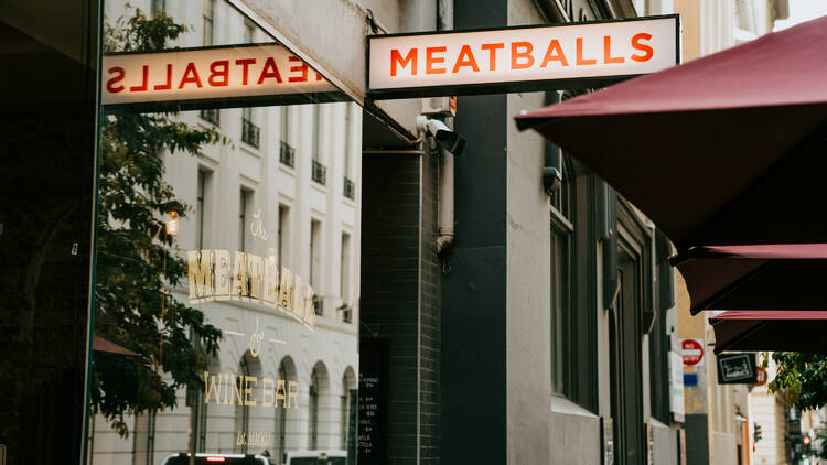 A back lit sign reading meatballs in capital red letters is out the front of the restaurant next to red umbrellas