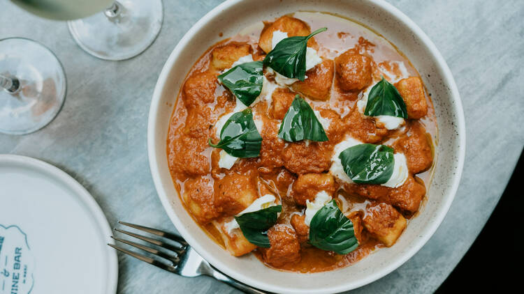 A plate of gnocchi in tomato sauce topped with cheese basil next to a silver fork
