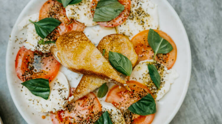 A caprese salad of mozzarella and sliced tomato with toasted bread sits on a white plate