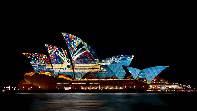 The sails of the Sydney Opera House illuminated by digital art at nighttime.