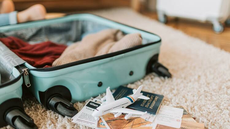An open suitcase next to a passport, some travel documents and a tiny toy plane.