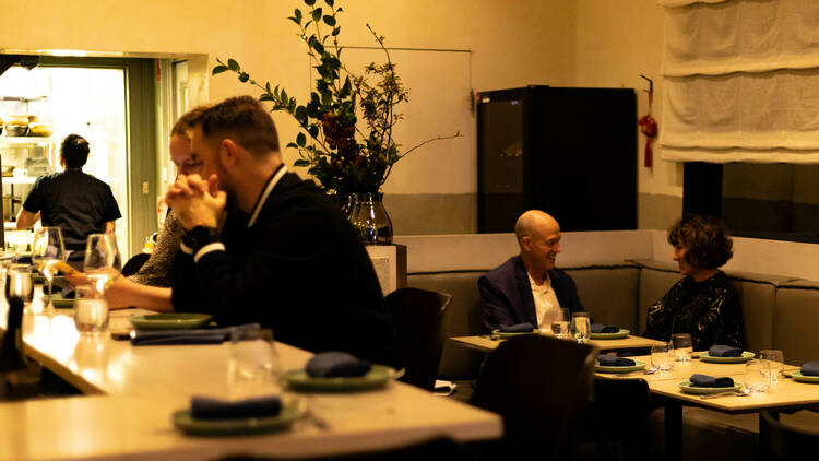 The dining room in Jeow includes bar seating and tables with banquettes in a golden lit room