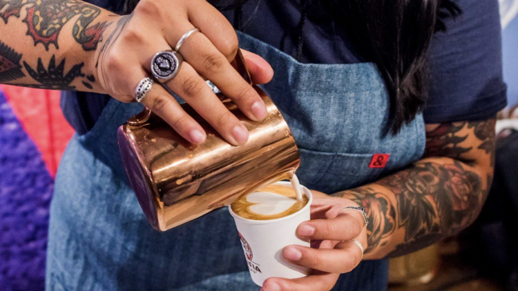 A barista pours a latte with heart-shaped latte art.