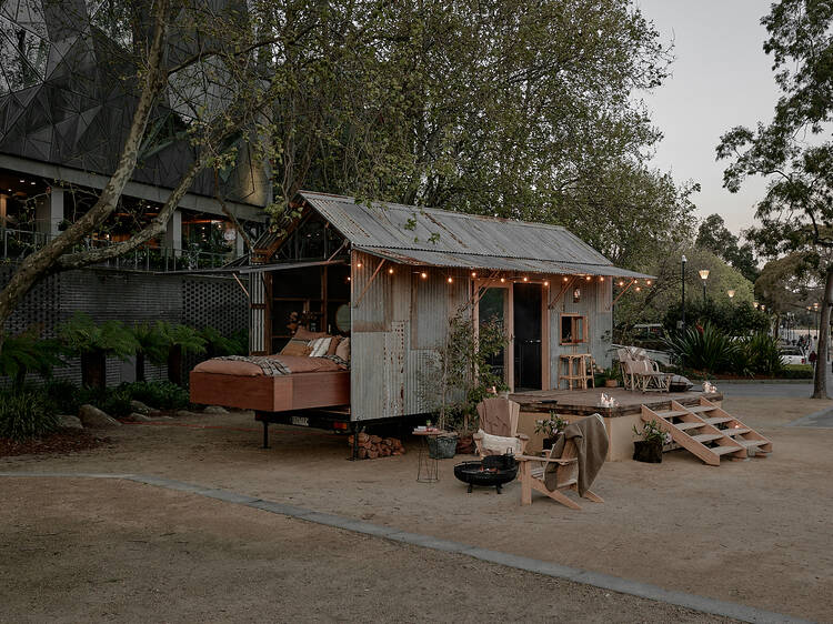 A tiny shed-like home with an outdoor bed, deck and bonfire station.