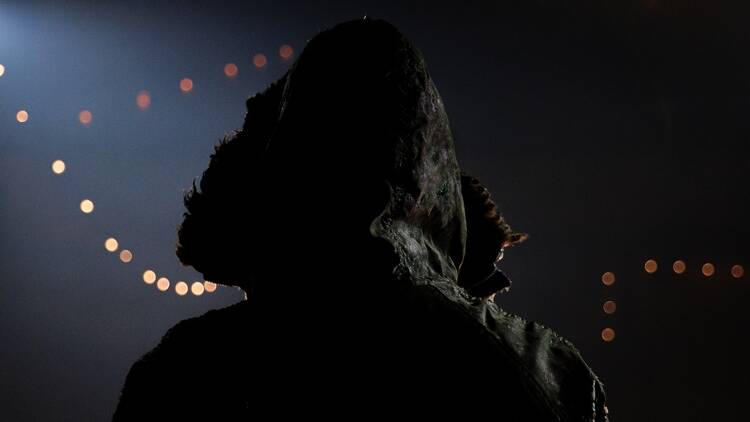The back of a figure wearing a hood in the dark