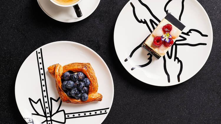 A black table with two coffees and two pastries on white plates