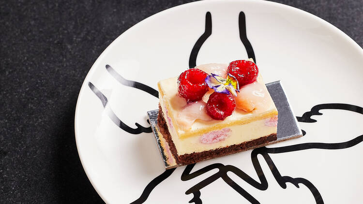 A cake topped with raspberries sits on a white plate on a black table