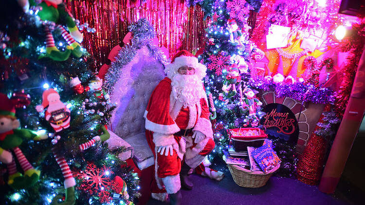 Santa Claus in a festive room with Christmas trees and presents.