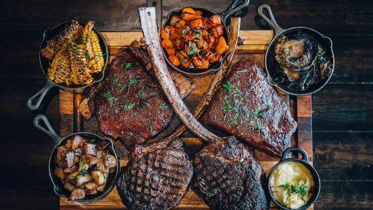 A selection of barbecued meats with charred corn, potatoes, mash and mushrooms