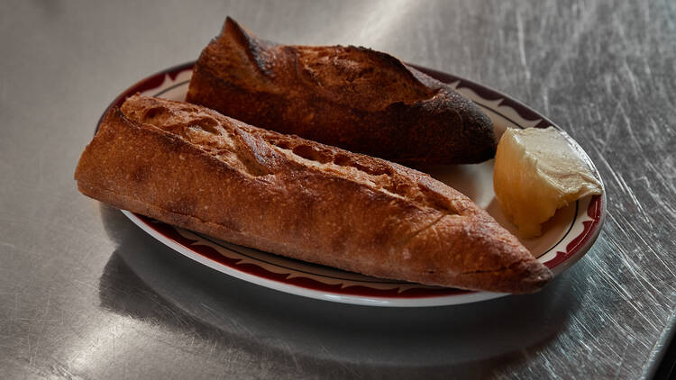 A plate has a baguette cut in half, next to a large dollop of butter on a silver bench