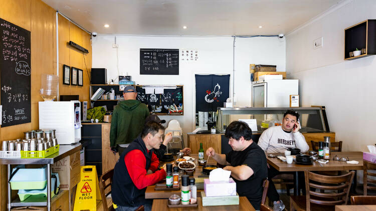 Inside Mr Lees there are wooden tables with different groups of people eating and someone paying at the counter