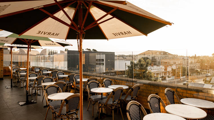 The rooftop bar has small tables and chairs and green and white umbrellas which say 'Harvie' on them