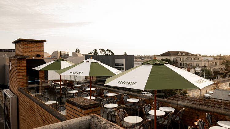 The rooftop bar at Harvie has small tables and white and green umbrellas and brick walls