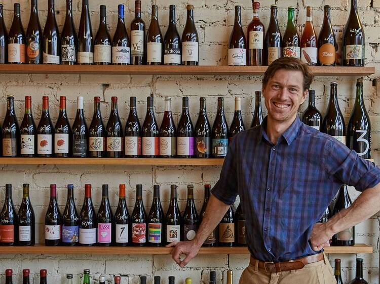 A bar owner with a wall of wine bottles