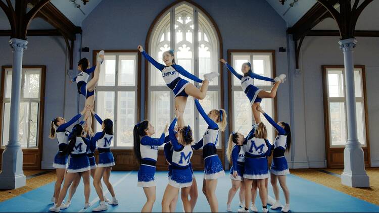 A group of cheerleaders in blue and white uniforms performing a routine in a church-like building.
