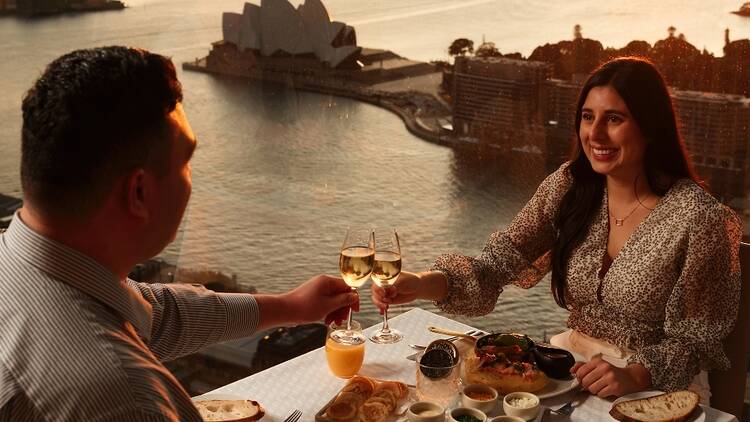 A man and a woman are enjoying a lobster omelette and Champagne at a restaurant with views of Sydney Harbour
