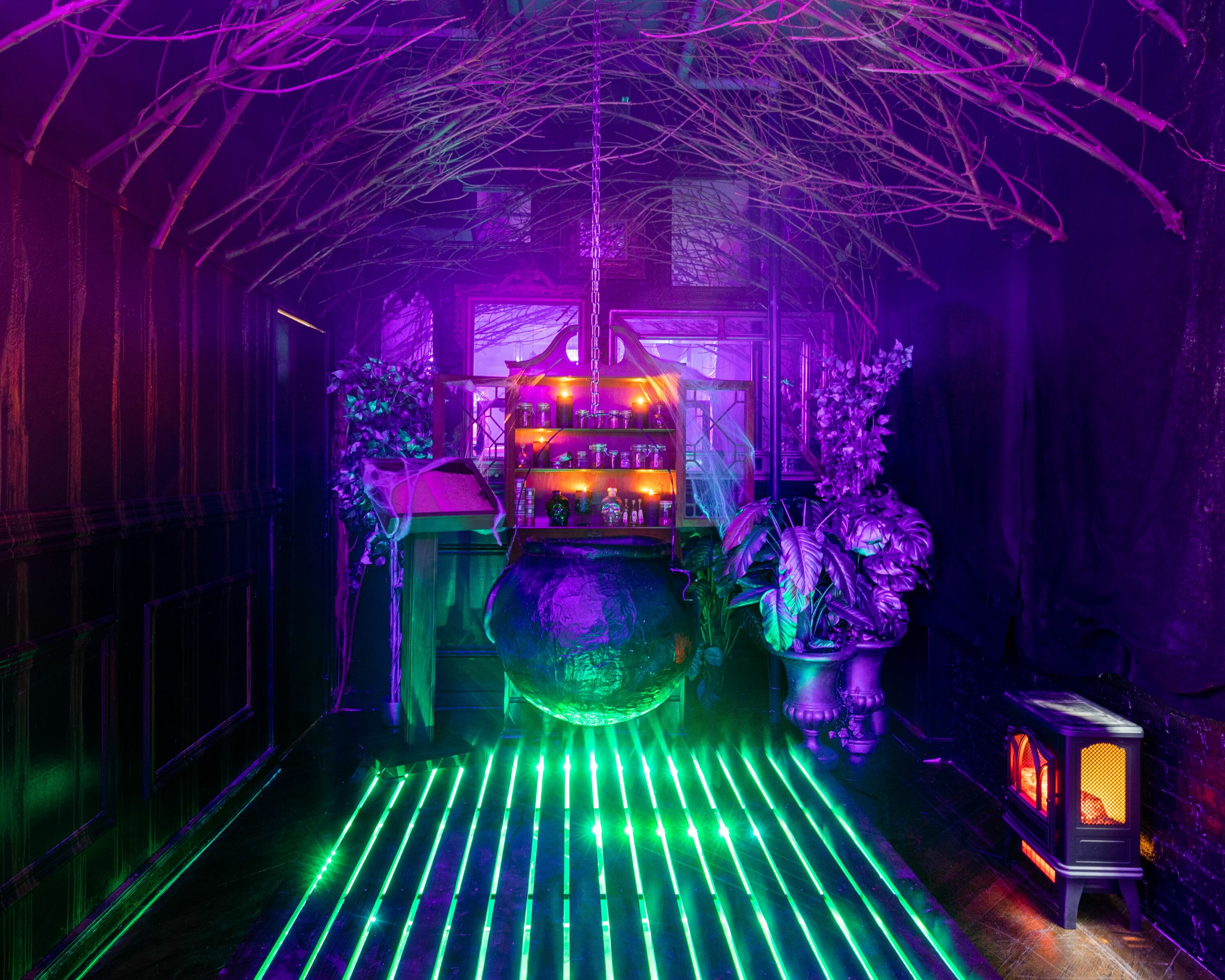 A room lit up with purple and green lights featuring a large cauldron, fireplace and Halloween-themed decor