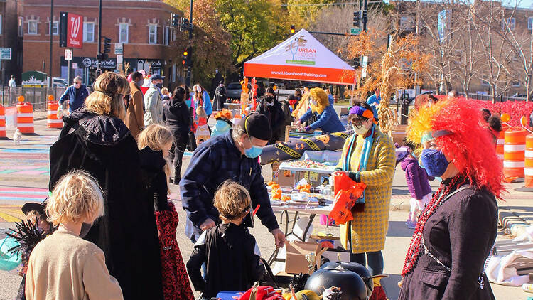 Costumed children visit a craft station manned by a woman in a red wig and black dress