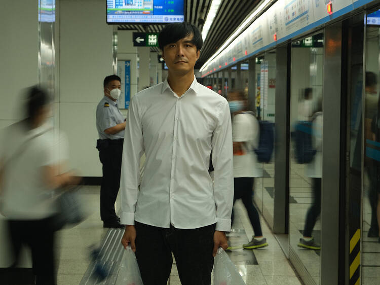 A man stands still in a train station, looking straight at the camera