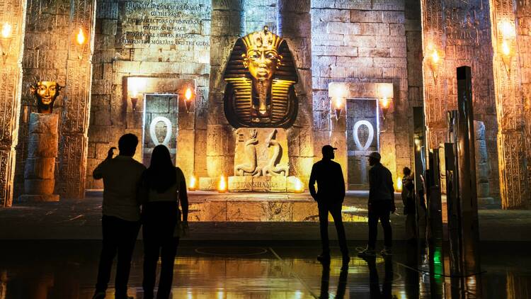 People look up at projections depicting King Tut's golden death mask in an ancient Egyptian tomb