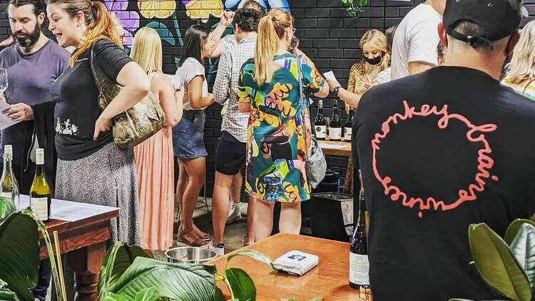 In a courtyard people gather around tables sampling different wines with graffiti mural on a black wall in the background