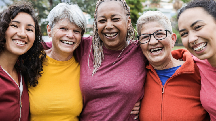 Five diverse women in bright clothes smile at the camera