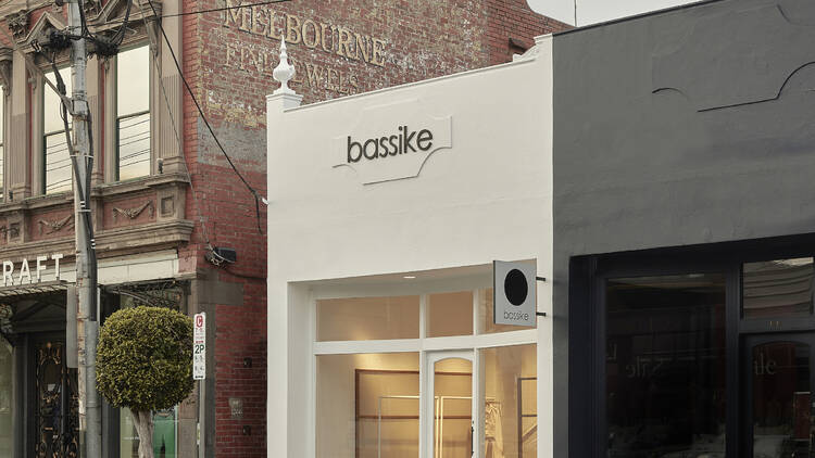 The store front on High Street is white with the words bassike on the top next to a black building and a brown building on the other side