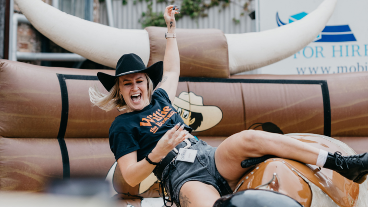A girl laughs while riding on a mechanical bull
