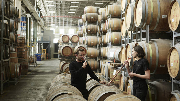 Two people stand inside a large warehouse filled with barrels of whiskey