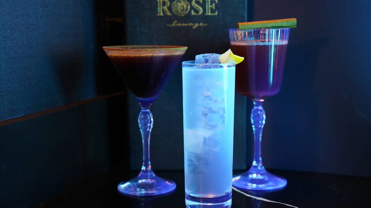 Three cocktails in front of a menu that reads 'Rose Lounge'