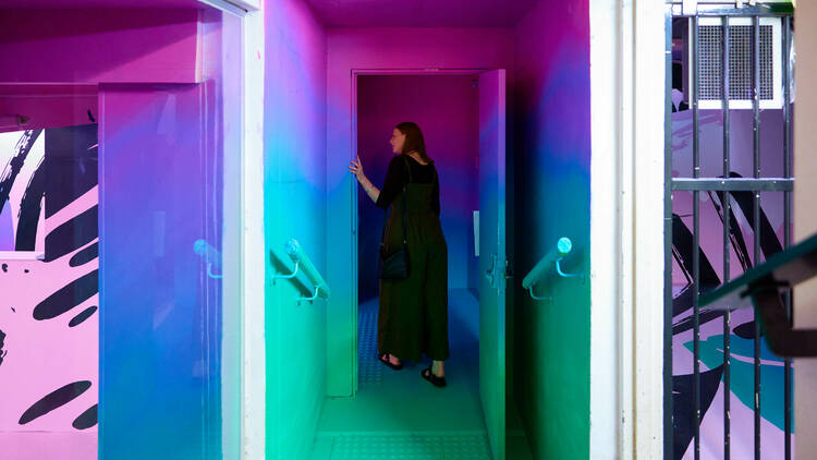 A woman walking through a multi-coloured painted doorway.