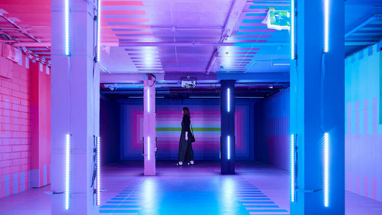 A woman walking through a space light up in purple, pink and blue lights.