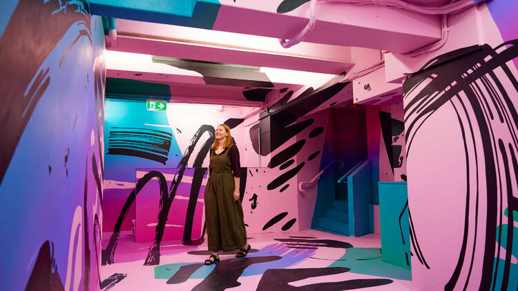A woman walking through a painted room with pink, black, blue and purple spirals.