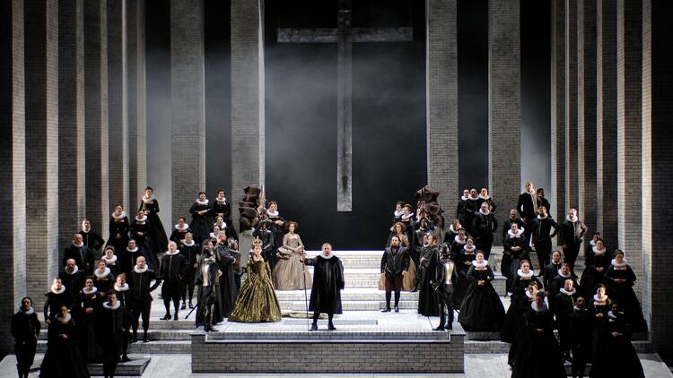 Performers in black outfits stand on a large stage during an opera performance of Don Carlos Performers in black outfits stand on a large stage during an opera performance of Don Carlos