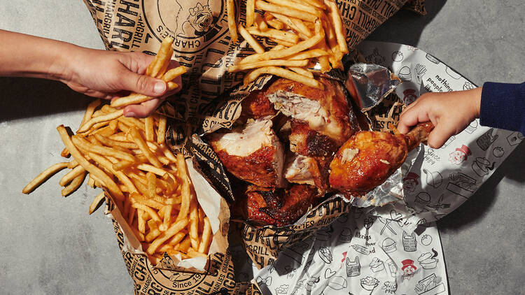 A birds eye view of take away bags of hot chops and chargrill chicken with someone reaching for a piece of chicken and some chips 