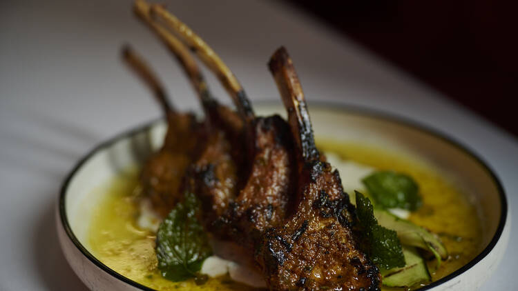 A white plate on a white table with grilled lamb in a yellow sauce 